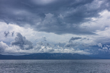 Stormy sky over mountains and sea. Dark dramatic clouds hang over the water surface, creating an atmosphere of tension and grandeur of nature. Podaca village, Makarska Riviera, South Dalmatia, Croatia