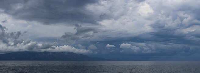 Stormy sky over mountains and sea. Dark dramatic clouds hang over the water surface, creating an atmosphere of tension and grandeur of nature. Podaca village, Makarska Riviera, South Dalmatia, Croatia