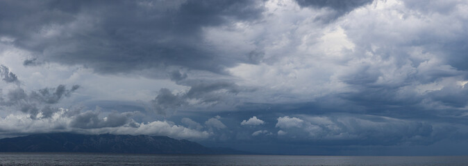 Stormy sky over mountains and sea. Dark dramatic clouds hang over the water surface, creating an atmosphere of tension and grandeur of nature. Podaca village, Makarska Riviera, South Dalmatia, Croatia