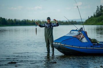 A satisfied fisherman holds fish on scales in a river