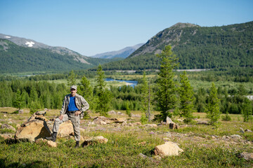 A hunter stands against the backdrop of a panorama of mountains and a forest 