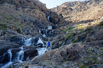 A hunter stands in a gorge next to a waterfall showing his thumbs up