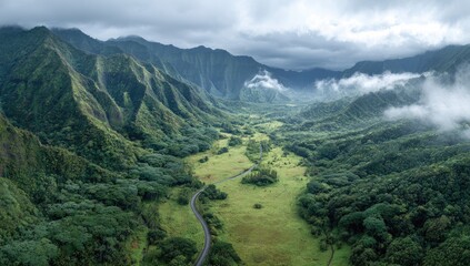 Fototapeta premium Lush green valley nestled between steep, cloud-shrouded mountains; a winding road traverses the verdant expanse