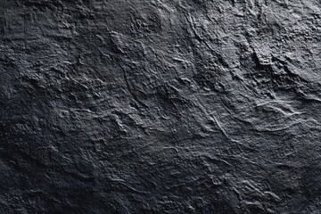 Dark, textured stone surface with uneven, rough, and slightly glossy surface showing varied shades of deep gray and black