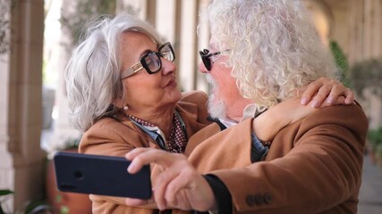 Delightful senior couple joyfully taking a selfie with a mobile phone, smiling and expressing affection for each other while capturing their happy moments together, celebrating life and love in a - Powered by Adobe