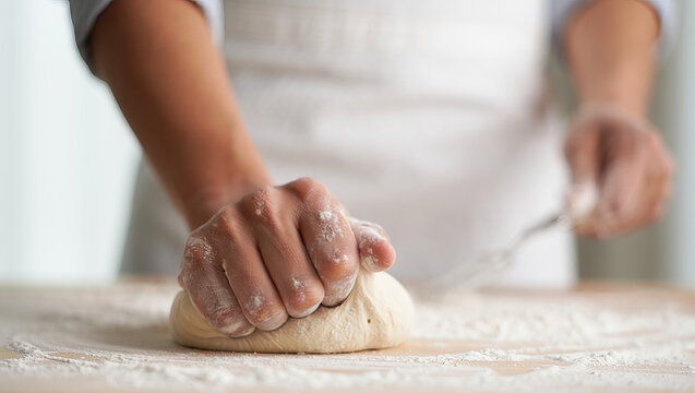Close-up of hands kneading dough, flour dust rising.