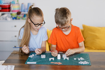 Fototapeta premium Boy and girl in glasses assembling constructor at school desk. Educational STEM activity for children developing creativity, teamwork, and problem-solving skills.