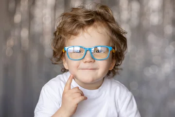 A close-up portrait of a little boy wearing eyeglasses with blue frames, looking cheerful and curious, highlighting his expressive eyes and joyful personality. © oes