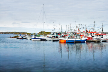 Fototapeta premium Quiet moment between departures and returns — colorful fishing boats rest in Andenes harbor, Northern Norway, embraced by calm waters and misty northern light.