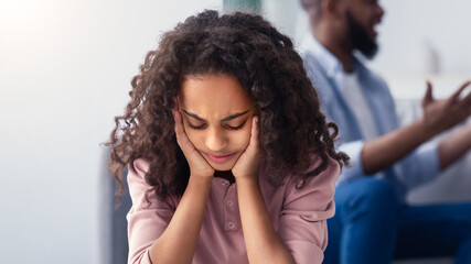 Family Conflicts. Sad little black girl covering ears with hands while her parents arguing in the...