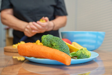 In a bright kitchen, a person prepares fresh vegetables including broccoli and carrots