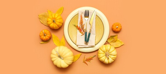 Beautiful table setting with fresh pumpkins and autumn leaves on orange background