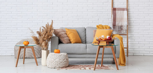 Grey sofa with autumn pumpkins and glowing candles in light living room