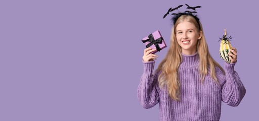 Happy young girl with Halloween pumpkin and gift on lilac background with space for text