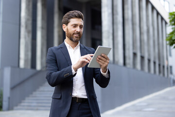 Smiling businessman using tablet device outdoors near modern office building