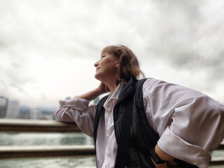 Middle-aged blonde woman enjoying her time on a waterfront in Hong Kong while reflecting on her travel adventure