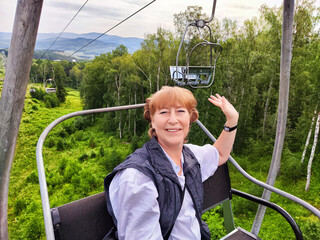 Middle-aged female traveler enjoying a scenic cable car ride through lush greenery in a picturesque...