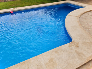 A pool with transparent blue water, surrounded by a wooden terrace and green grass. Swimming pool steps in bright blue water. Pool with blue water. Beautiful water in a swimming pool 1.
