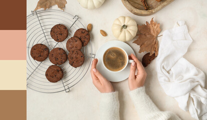 Female hands with cup of tasty pumpkin coffee, autumn decorations and cookies on white grunge background, top view