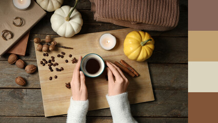 Female hands with cup of tasty pumpkin coffee, autumn decorations, books and warm sweater on brown wooden background, top view