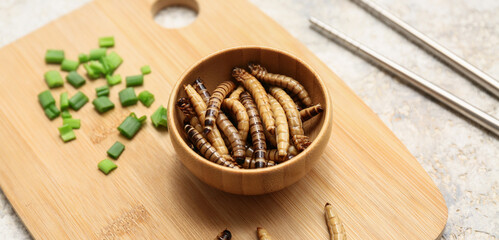 Wooden bowl with fried maggots and green onion on white background