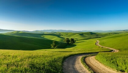 a winding dirt road leads through a lush green field under a clear blue sky the landscape features rolling hills and distant trees