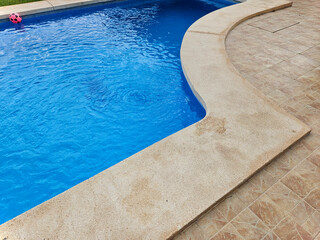 Highlights, sparks, ripples on the surface. There are fountain streams around the perimeter. Relax in the backyard of a country house. Part of swimming pool with blue water. Water swimming pool.