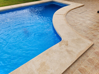 Private blue swimming pool detail with green small tree. Swimming pool edge with ladder in home. Entretien piscine. Swimming pool. Private swimming pool by the garden. Une belle piscine.