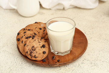 Wooden plate of sweet cookies with chocolate chips and glass of milk on white background