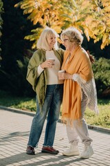 Two senior women enjoying coffee and conversation in autumn park