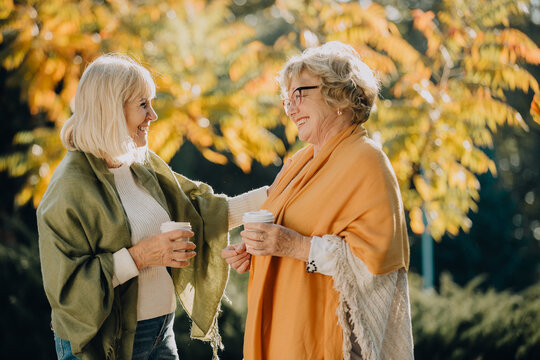 Two senior women enjoying a hot drink together in autumn park