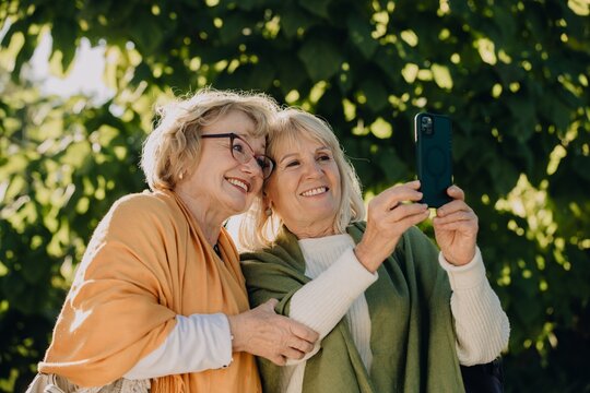 Two senior women taking a selfie in the park, embracing friendship and technology