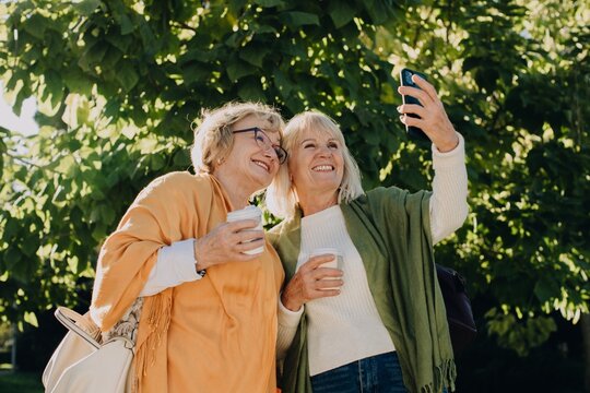 Two senior women taking a selfie while enjoying coffee outdoors