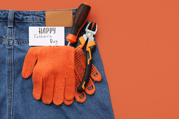 Jeans with tools, gloves and greeting card with text HAPPY FATHER'S DAY on orange background