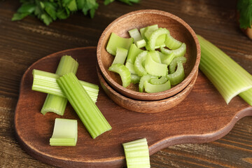 Board and bowl with cut fresh green celery on wooden background