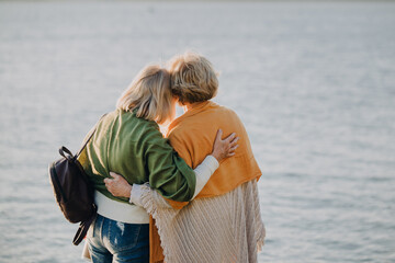 Two senior women embracing friendship by the lake