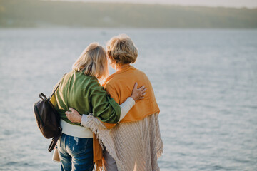 Two senior women embracing friendship by the lake at sunset