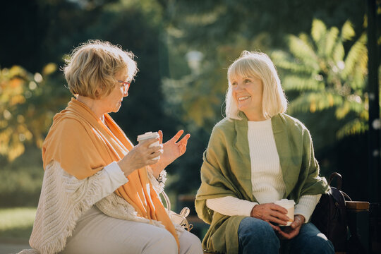 Two senior women enjoying coffee and conversation in park - Powered by Adobe