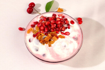 Bowl of pomegranate yogurt with pomegranate pieces, raisins and fresh cow cream for healthy eating on light table. Healthy breakfast with ingredients, kitchen background, Natural nutrition concept.