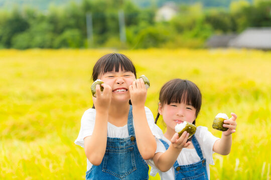 田んぼの前でおにぎりを持つ姉妹