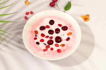 Fruit yogurt with cherry, pomegranate, raisins and fresh cow's cream for healthy eating on elegant table. Healthy breakfast with ingredients, kitchen background. Natural nutrition and diet concept.
