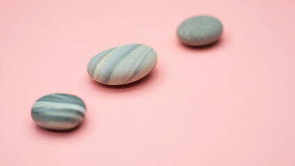 Three smooth stones arranged on a soft pink background for zen and relaxation