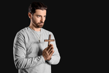 Religious man with cross praying on black background