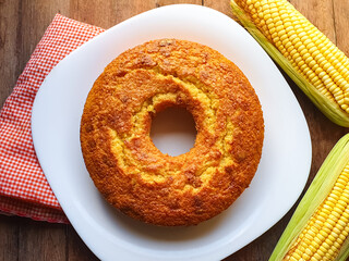 golden corn cake on a white plate on a wooden background with corn around