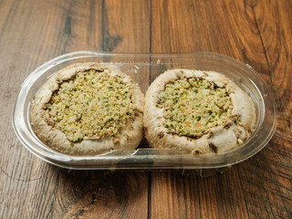 Two stuffed mushrooms in a plastic package on wooden background. Fine meal made of natural ingredients. Agriculture and farming, Food industry