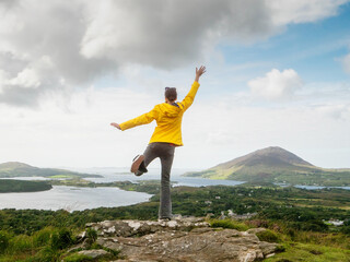 A woman in a yellow jacket is standing on a mountain top, looking out over a beautiful landscape. She is happy and content, enjoying the view and the fresh air. Concept of freedom and adventure