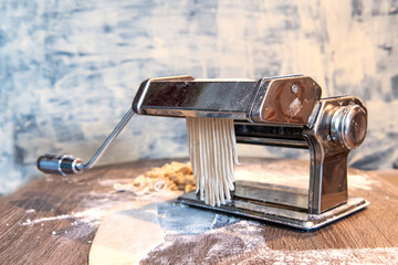 Chrome Pasta Machine Rolling Fresh Tagliatelle on Wooden Kitchen Surface