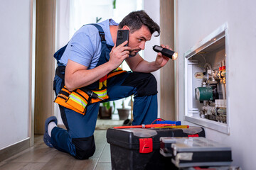 Handyman conducts household repairs while checking heating system with flashlight and phone