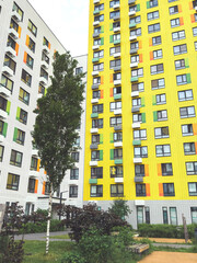 Tall modern apartment building with yellow and white facade and colored accents, surrounded by...