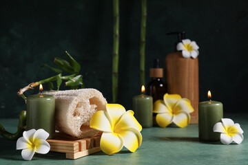 Beautiful spa composition with loofah sponge, plumeria flowers and burning candle on green grunge...